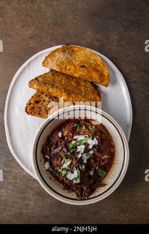 A plate of Mexican beef birria tacos of shredded beef, onions, guajillo peppers, cilantro, and broth with dipping sauce juices Stock Photo