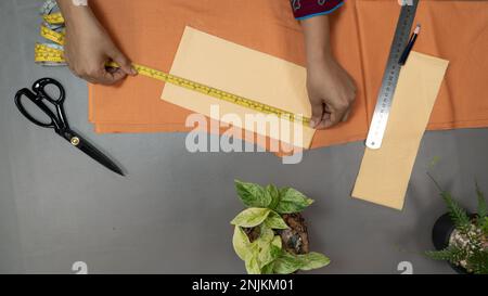 Hand measuring fabric with tape on a gray background. sewing project top view Stock Photo