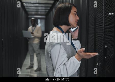 Phone call, technician and woman in a server room for maintenance, repairs or data analysis. Systems, technology and Asian female engineer on mobile Stock Photo