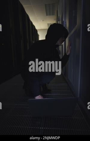 Hacking, server room and person on laptop for coding software, data center crime and cyberpunk in dark. Network hacker, woman or user in cybersecurity Stock Photo