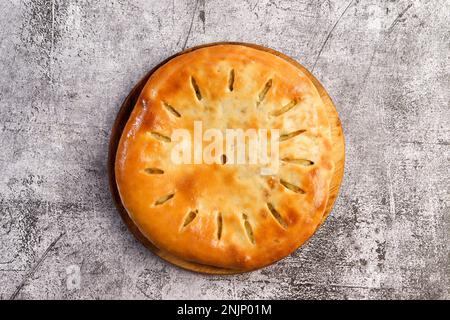 Traditional Ossetian pie with mashed potatoes and herbs on a cutting wooden board on a dark grey background. Top view, flat lay Stock Photo