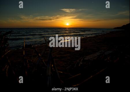 Romantic sunset by the sea, the sun almost at the sea horiznt the cloudy sky shines in intense gold orange colors, in the foreground in the shade bran Stock Photo