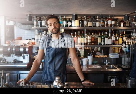 The best bar by far. Portrait of a confident young man working behind a bar counter. Stock Photo