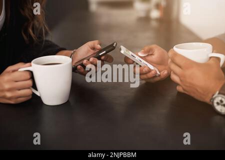 Starting the day with coffee and social media. a young couple using their mobile phones and having coffee at home. Stock Photo