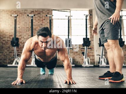 Fighting fit. two fit and determined young men doing pushups one by one inside of a gym. Stock Photo
