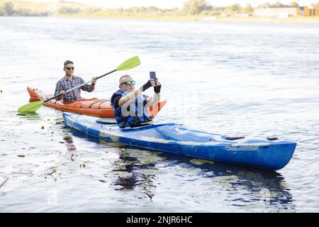 Kayaking on the river. Two young men sit in kayaks and take a selfie with a portable camera. The concept of water entertainment. Stock Photo