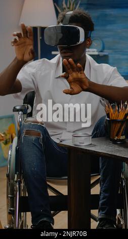 Disabled african american man using vr glasses for inspiration and virtual drawing in workshop studio. Black young artist in wheelchair with technology for modern masterpiece process Stock Photo