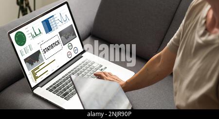 Laptop Computer Showing Statistical Infographics Stands on a Desk in the Living Room. In the Background Cozy Living Room. Stock Photo