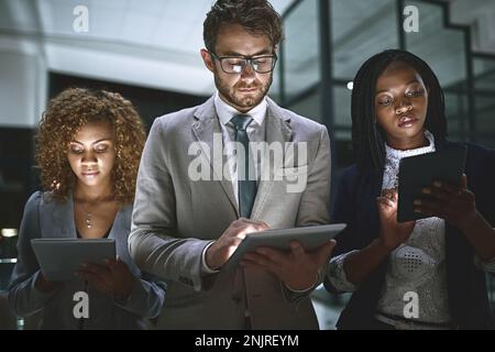 Dedication keeps them performing no matter the hour. a group of businesspeople working late on digital tablets in an office. Stock Photo