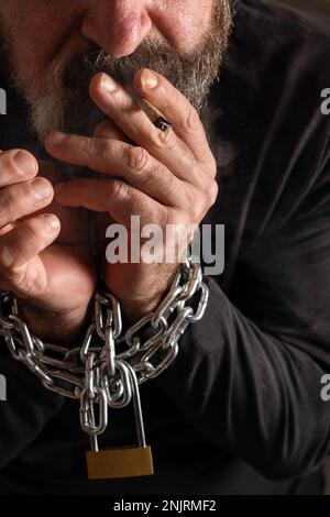 guy chained to a cigarette man with a cigarette in his mouth and his hands chained together, addiction  concept, black background Stock Photo