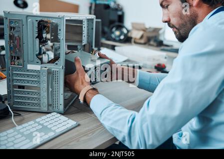 Engineering, technician and man fixing the hardware of a computer in workshop or office. IT, technology and male professional doing maintenance or Stock Photo