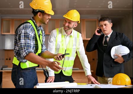 Professional Caucasian male construction engineer manager talking and planning building process with an Asian male construction inspector while a Cauc Stock Photo