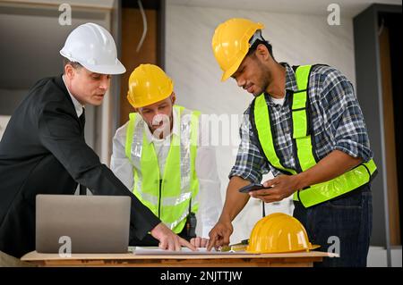 Professional Asian male foreman in uniform and yellow safety hat is talking and planning building process with a Caucasian businessman and constructio Stock Photo