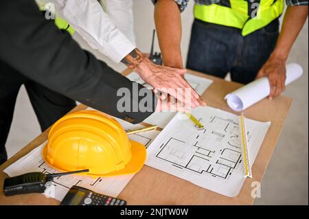 Cropped image of a team of construction workers and a businessman putting their hands together over the working table, showing spirit, teamwork. top v Stock Photo