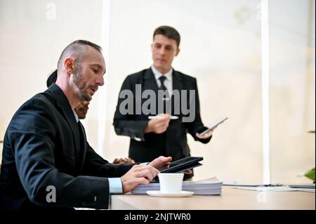 Professional Caucasian businessman or male financial worker using a digital tablet while listening to his boss's conference in the meeting. side view Stock Photo