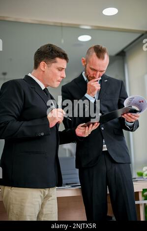 Two smart and thoughtful Caucasian businessmen are analyzing and examining financial data on a report, working together in the office. Stock Photo