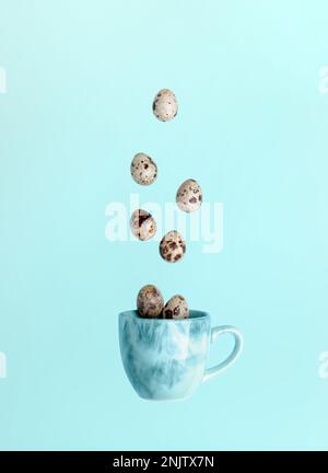 Easter minimal creative card. Quail eggs and falling to blue cup on light blue background. Falling food image. Creative advertising of healthy food. T Stock Photo