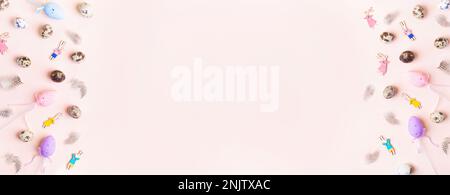 Easter wide pastel pink banner. Top view of frame of festive decorations. Flat lay colorful wooden bunnies, eggs, feathers on pink paper. Holiday card Stock Photo