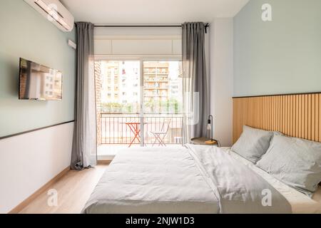Spacious bright room with bed, large opening on entire wall with sliding plastic doors and access to balcony. Room has table with chair, air Stock Photo