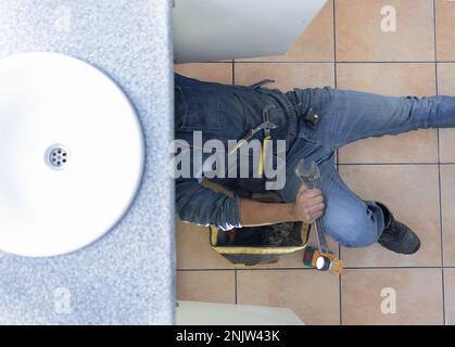 Top view, plumber and man on floor in kitchen for maintenance service, engineering or home renovation. Above of handyman, plumbing and contractor with Stock Photo