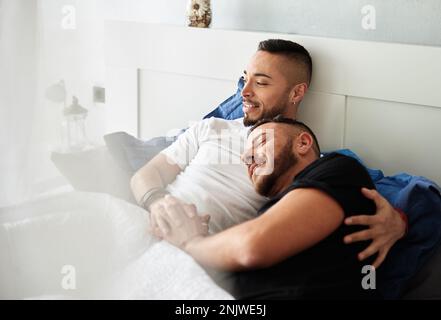 Male couple enjoying together and smiling while relaxing in bed at home. Stock Photo