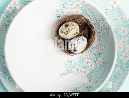 Two quail eggs in nest on light blue plates with gentle floral pattern. Romantic festive Easter mock up on plate. Holiday table setting. Congratulatio Stock Photo
