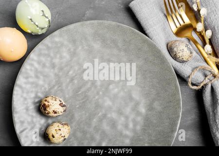 Round empty textured gray plate, cutlery, quail eggs, candles on gray. Easter table setting. Happy Easter holiday advertisements for cafes and restaur Stock Photo