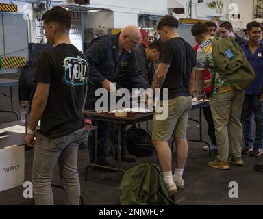 U.S. Navy Sailors check in simulated American citizens during a non-combatant evacuation operation training aboard the Amphibious Assault Ship USS Tripoli (LHA-7) in the Philippine Sea, Aug. 10, 2022. NEO training ensures the Tripoli Amphibious Ready Group is ready to receive American citizens if they need to be evacuated from a foreign country. The 31st MEU is operating aboard ships of the Tripoli ARG in the 7th Fleet area of operations to enhance interoperability with allies and partners and serve as a ready response force to defend peace and stability in the Indo-Pacific region. Stock Photo