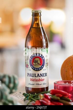 Paulaner beer bottle placed near candle and red peppers in light kitchen against blurred background Stock Photo