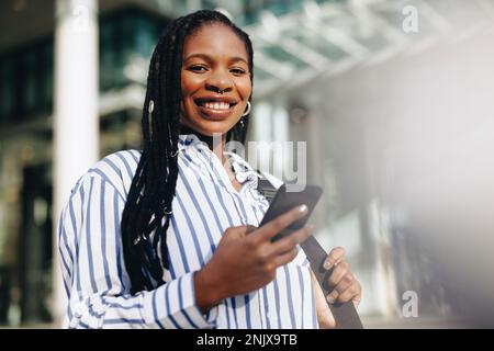 Young business woman smiling at the camera while commuting to her office in the city. Portrait of a happy young business woman using a smartphone on h Stock Photo