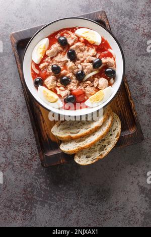 Murcian Salad La ensalada murciana with tomato, canned tuna, black olive, egg and onion closeup on the plate on the wooden board. Vertical top view fr Stock Photo