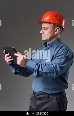 Engineer in hardhat doing planning digitally with a tablet, isolated on gray background Stock Photo