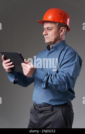 Engineer in hardhat doing planning digitally with a tablet, isolated on gray background Stock Photo
