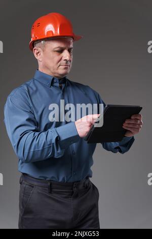 Engineer in hardhat doing planning digitally with a tablet, isolated on gray background Stock Photo