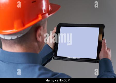 Engineer in hardhat doing planning digitally with a tablet, isolated on gray background Stock Photo