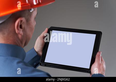 Engineer in hardhat doing planning digitally with a tablet, isolated on gray background Stock Photo