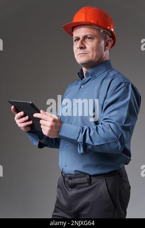 Engineer in hardhat doing planning digitally with a tablet, isolated on gray background Stock Photo