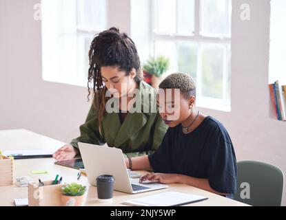 College students working together two young women friends brainstorming ideas for project sitting at desk using laptop computer in class Stock Photo