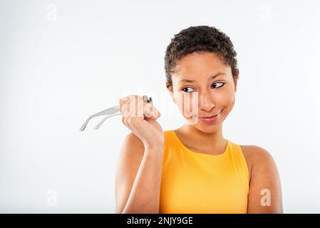Positive young ethnic female model in yellow top with short curly hair touching glasses and looking away against white background Stock Photo