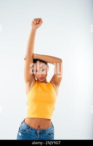 Attractive young African American female in stylish outfit raising arms while posing in studio during photo shoot on white background Stock Photo