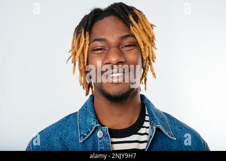 Smiling young African American man with dreadlocks in denim jacket and hat looking at camera on white background Stock Photo