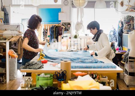 Focused female tailors in casual clothes preparing pattern while working with colorful fabric in atelier Stock Photo