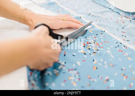 Anonymous designer using scissors to cut fabric while working in atelier with patterns Stock Photo