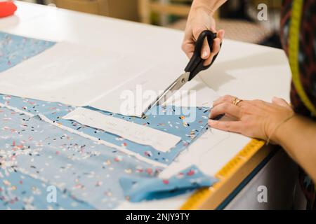 Anonymous designer using scissors to cut fabric while working in atelier with patterns Stock Photo