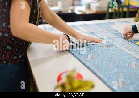 Anonymous designer using scissors to cut fabric while working in atelier with patterns Stock Photo