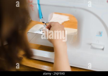 Unrecognizable female tailor putting thread into sewing machine while working in light atelier Stock Photo