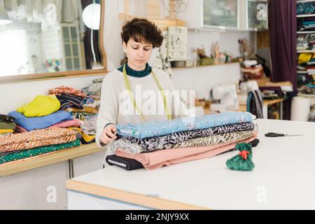 Female designer in casual clothes with measuring tape around neck standing with colorful textile in atelier Stock Photo