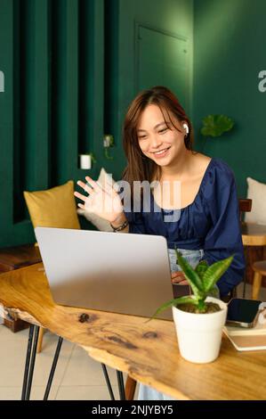 positive young freelancer waving hand while calling waiter in cafe ...