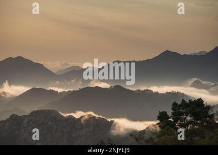 Picturesque scenery of silhouettes of high mountains covered with thick clouds under sunset sky in Asturias Stock Photo
