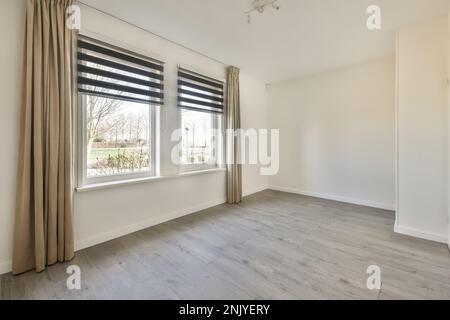 Windows with curtains on white wall of sunlit empty room of new house in daytime Stock Photo